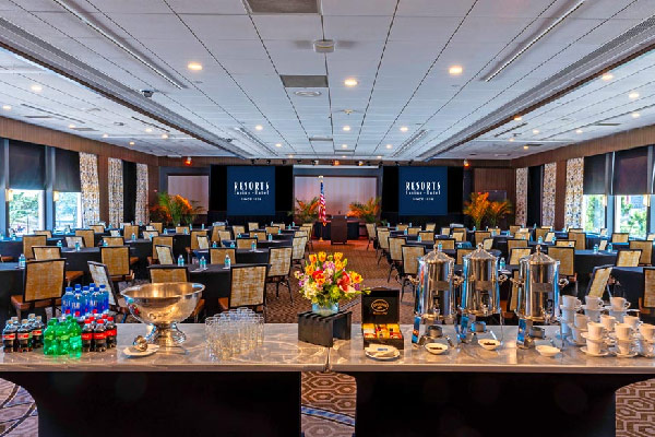 Conference ballroom with classroom seating, a stage, and a refreshment table in the foreground.