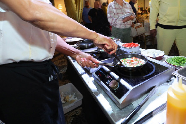 A chef cooks a dish in a pan on a portable burner, stirring ingredients at a buffet station.