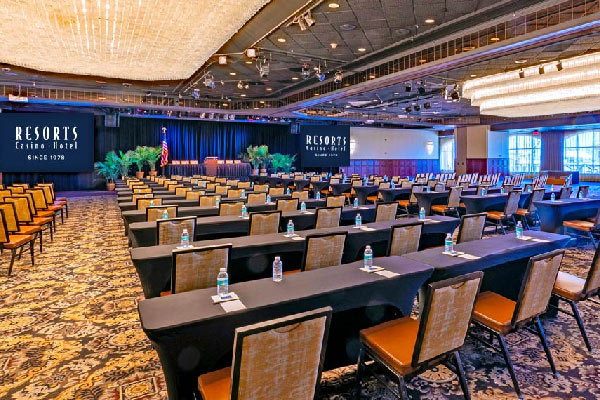 Conference room set with long tables, chairs, bottled water, and a stage at the front.