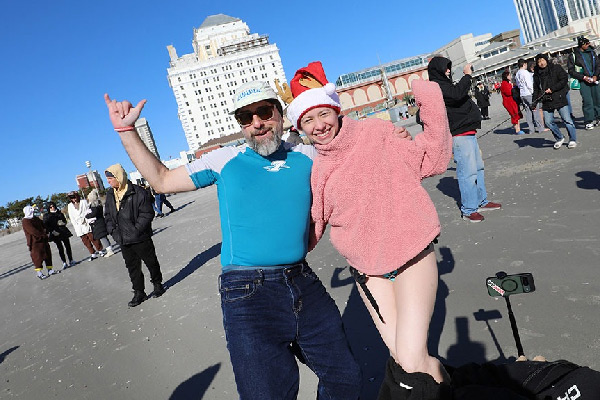 Two smiling adults pose arm-in-arm, wearing cold-weather outfits and a Santa hat, celebrating.