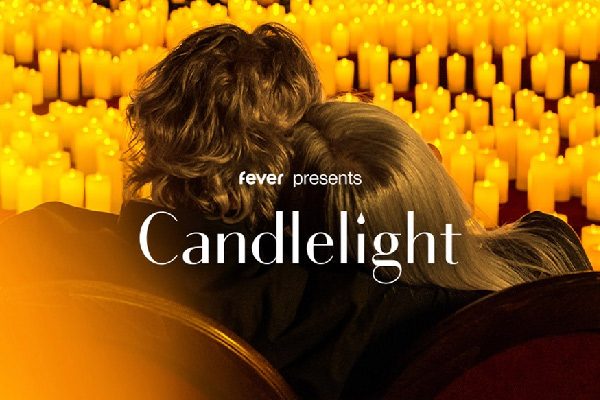 Promotional image for Fever’s Candlelight concert, showing a couple embracing while seated among glowing candles.