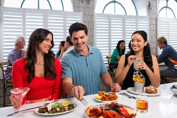 A group of people sit at a table, enjoying lobster and other food.