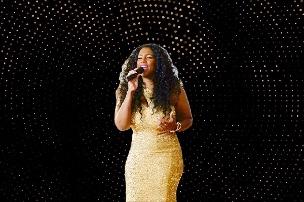 a singer in a gold dress performing with a microphone against a dark, starry backdrop.